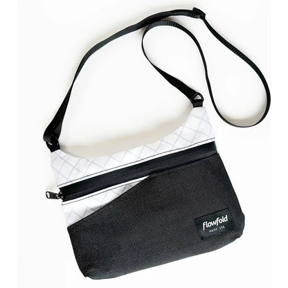 A top-down view of the Flowfold Eclipse Crossbody bag in Jet Black with a white upper section and black strap against a white background.