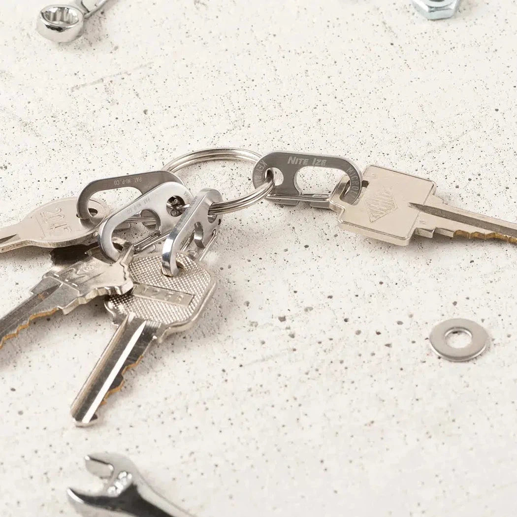 A close-up of the Nite Ize KeyRing MicroLink on a speckled surface with keys and a wrench visible.