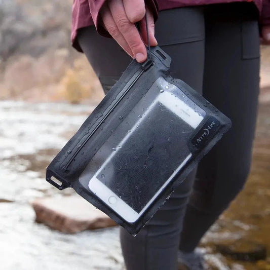 A hand holds the Nite Ize RunOff Waterproof Pocket with a smartphone inside, against a rocky outdoor background.