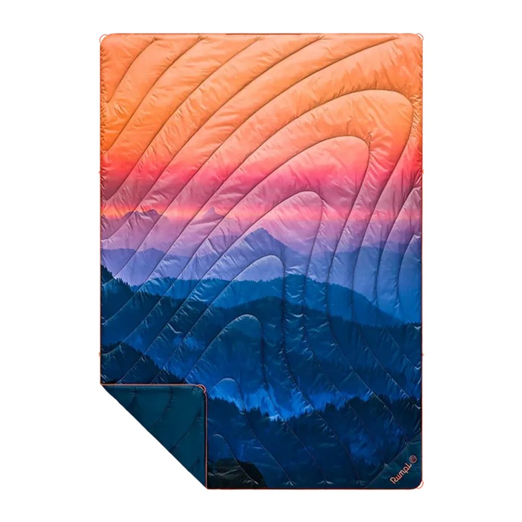 A Rumpl Original Puffy blanket in Alpenglow color shows a mountain sunset design with a folded corner visible.