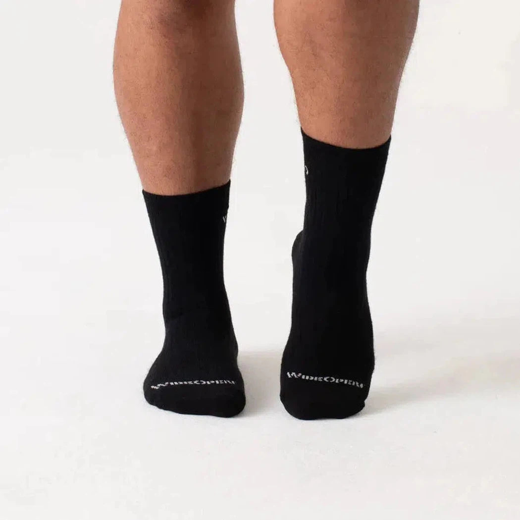 Back view of black Wide Open Men's Solid Cushioned Micro Crew Socks on a person against a white background.